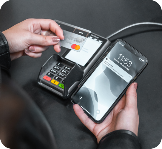 A person pays with a card at a point-of-sale terminal and simultaneously receives a notification on their mobile screen for a digital receipt.