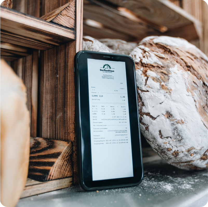 Ein vor einem Laib Brot platziertes Handy zeigt einen digitalen Kassenbon im PDF Format